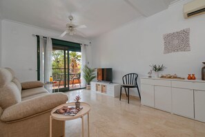 Ein modernes Wohnzimmer mit einer Couch, einem kleinen Tisch, einem Fernseher und einem Essbereich mit Stühlen und einem Tisch.