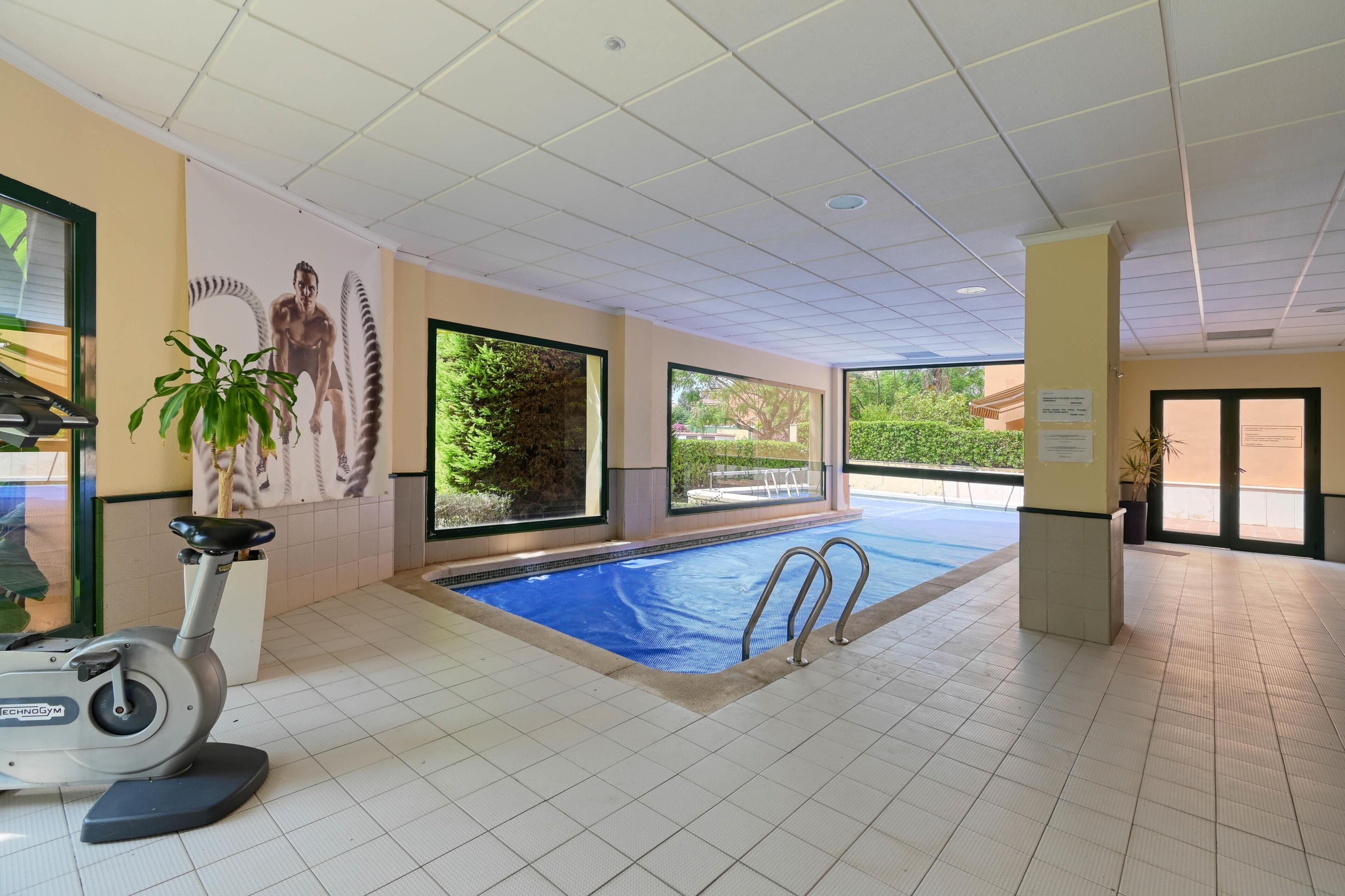 An indoor swimming pool with a stationary bike, large windows, and a view of the outdoors.