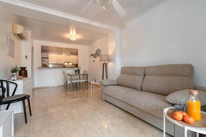 Ein modernes Wohnzimmer mit einer Couch, einem Esstisch mit Stühlen, einem kleinen Beistelltisch mit Orangensaft und Orangen sowie einer Lampe.