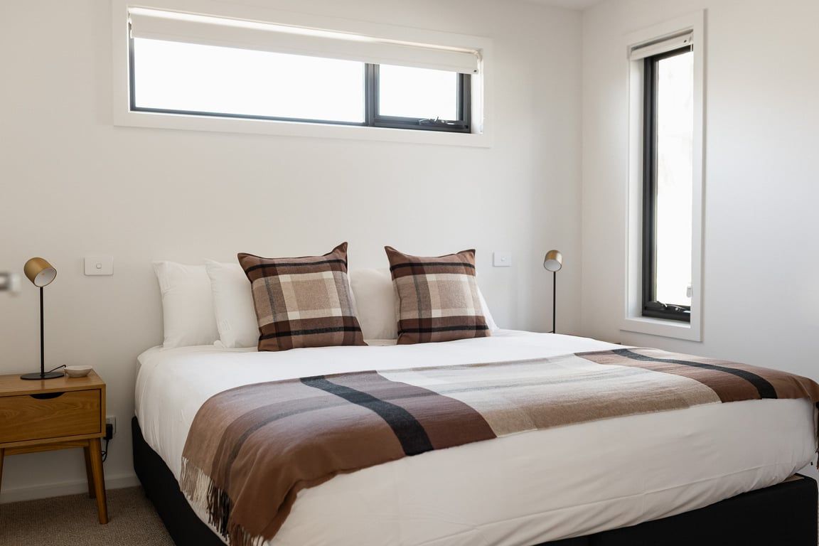 A bedroom with a bed, two bedside tables, a window, and a wall-mounted light fixture.