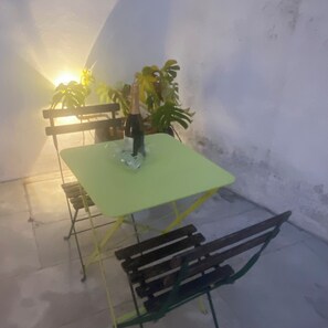 A table with a bottle, a chair, and a potted plant in a room with a plain wall.