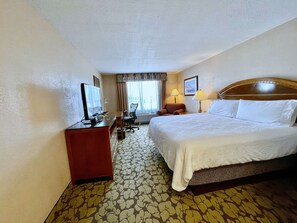 Een hotelkamer met een bed, bureau, stoel, televisie en een kamerbreed tapijt met dessin.