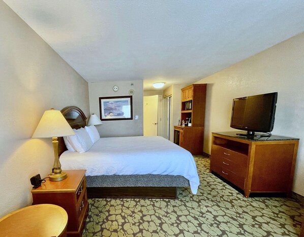 Een hotelkamer met een bed, een bureau met lamp, een televisie en een kledingkast.