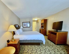A hotel room with a bed, a desk with a lamp, a television, and a wardrobe.