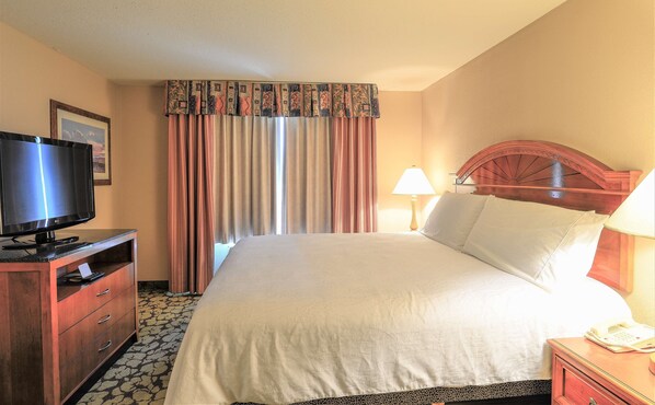 A hotel room with a bed, a TV, a desk with drawers, a lamp, and a telephone.