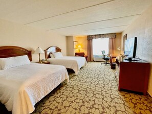 A hotel room with two beds, a desk, a chair, a television, and a window with curtains. - Houston Hideaway | Pool + Free Breakfast  & Parking | CityCentre - 5.8 miles (Houston)