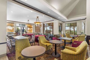 Een ruime, overdekte eethoek met meerdere tafels en stoelen, grote ramen en een plafond met inbouwverlichting.