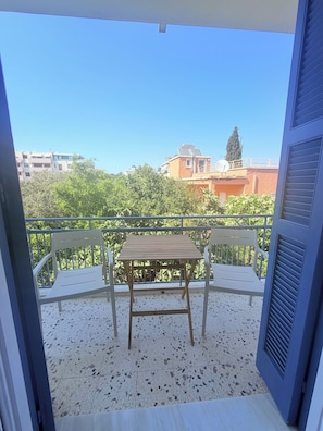 A balcony with a table and two chairs, a clear view of the surrounding buildings, and a green hedge. - Blu Windows Rhodes (Rodos)