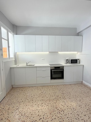 A compact kitchen with white cabinets, a microwave, and a built-in oven. - Blu Windows Rhodes (Rodos)