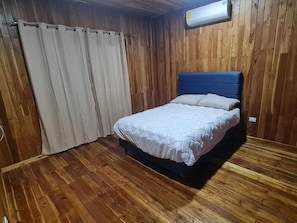 A bedroom with a bed, wooden walls, and a ceiling-mounted air conditioning unit. - Las Brisas House (Nicoya)