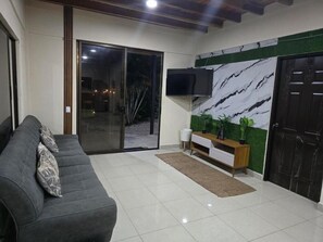 A living room with a sofa, a flat-screen TV, a wooden cabinet, and a sliding glass door leading to an outdoor area. - Las Brisas House (Nicoya)