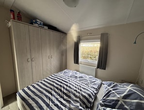 Un dormitorio con cama, armario, ventana con cortinas y radiador.