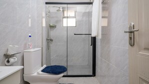 A modern bathroom with a glass-enclosed shower, a toilet with a blue mat, and a towel rack. - Diamond Homes Kileleshwa (Nairobi)