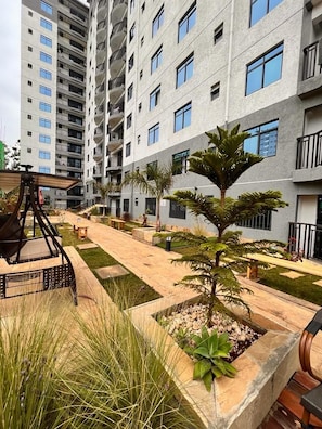 Un edificio residencial de varios pisos con balcones, un patio con asientos y plantas en macetas.