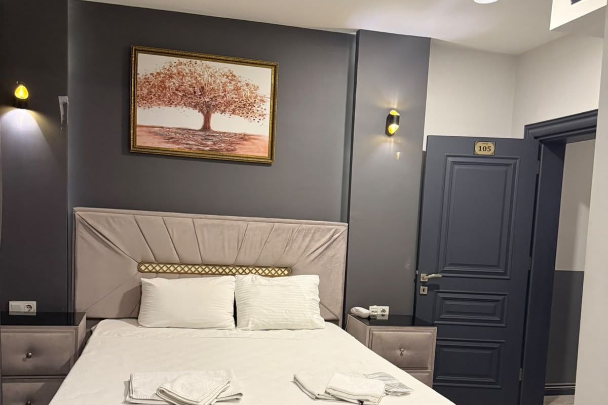 A hotel room with a large bed, bedside tables, a nightstand, a door, and a wall-mounted picture.