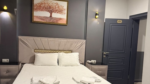 A hotel room with a large bed, bedside tables, a nightstand, a door, and a wall-mounted picture. - uckun palas (fatih)