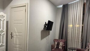 A hotel room with a bed, a television mounted on the wall, a chair, and a small table. - uckun palas (fatih)