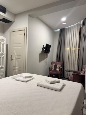 Ein Hotelzimmer mit einem Bett, einem an der Wand montierten Fernseher, einem Sessel und einem kleinen Tisch.