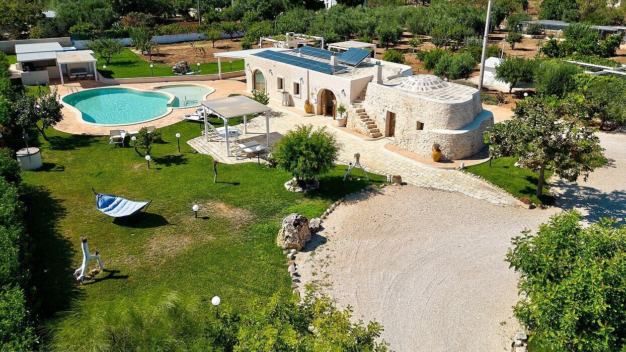 A property with a swimming pool, outdoor seating, and a stone building with a flat roof.