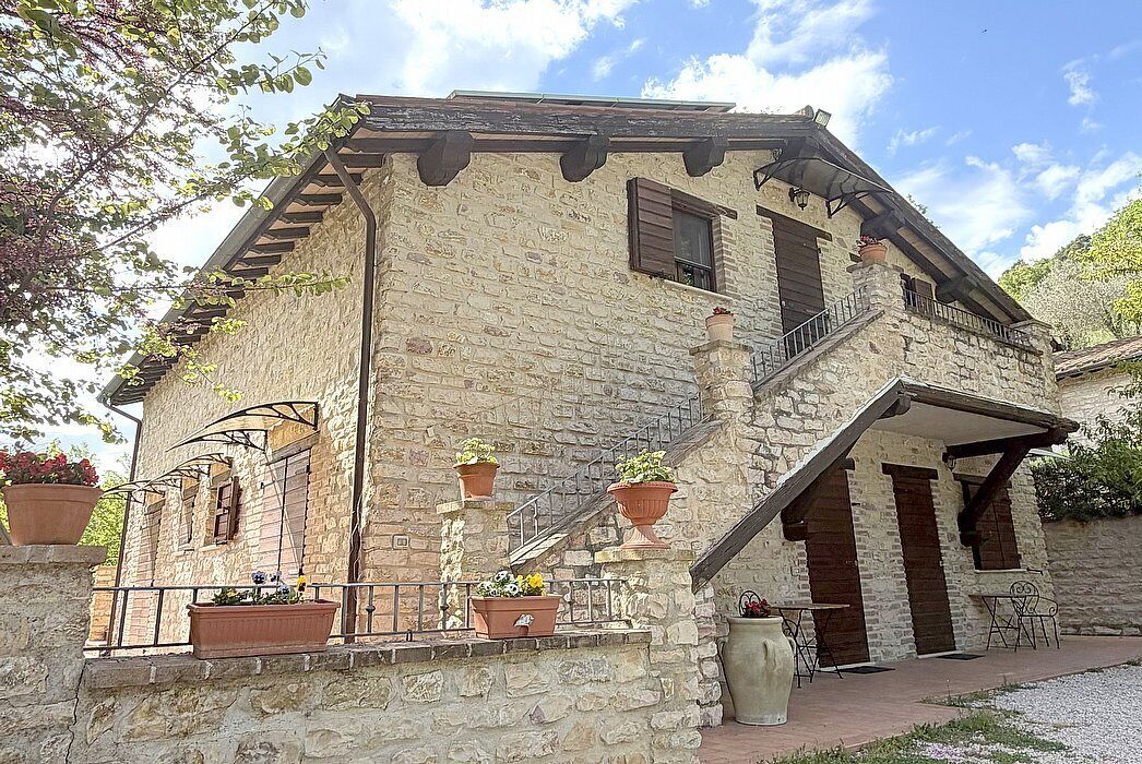 Un edificio in pietra con un balcone, piante in vaso e posti a sedere all'aperto.