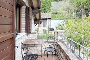 A wooden balcony with a table and chairs, a stone wall, and a view of a house and trees. - Casa Fronda A: A graceful apartment that is part of an ancient country house situated at a short distance from the shores of Lake Piediluco, with Free WI-FI. (Terni)