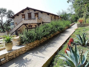 A stone building with a sloped roof, a staircase leading to a balcony, and a pathway lined with plants. - Casa Fronda A: A graceful apartment that is part of an ancient country house situated at a short distance from the shores of Lake Piediluco, with Free WI-FI. (Terni)