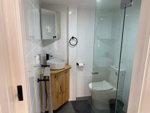 Een moderne badkamer met een houten wastafelmeubel, een witte wastafel, een douchecabine met glazen wanden en een toilet.