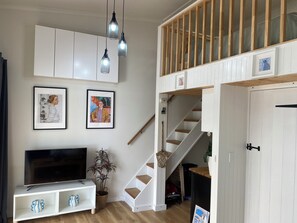 A living room with a TV, white cabinets, framed artwork, a staircase, and a plant.