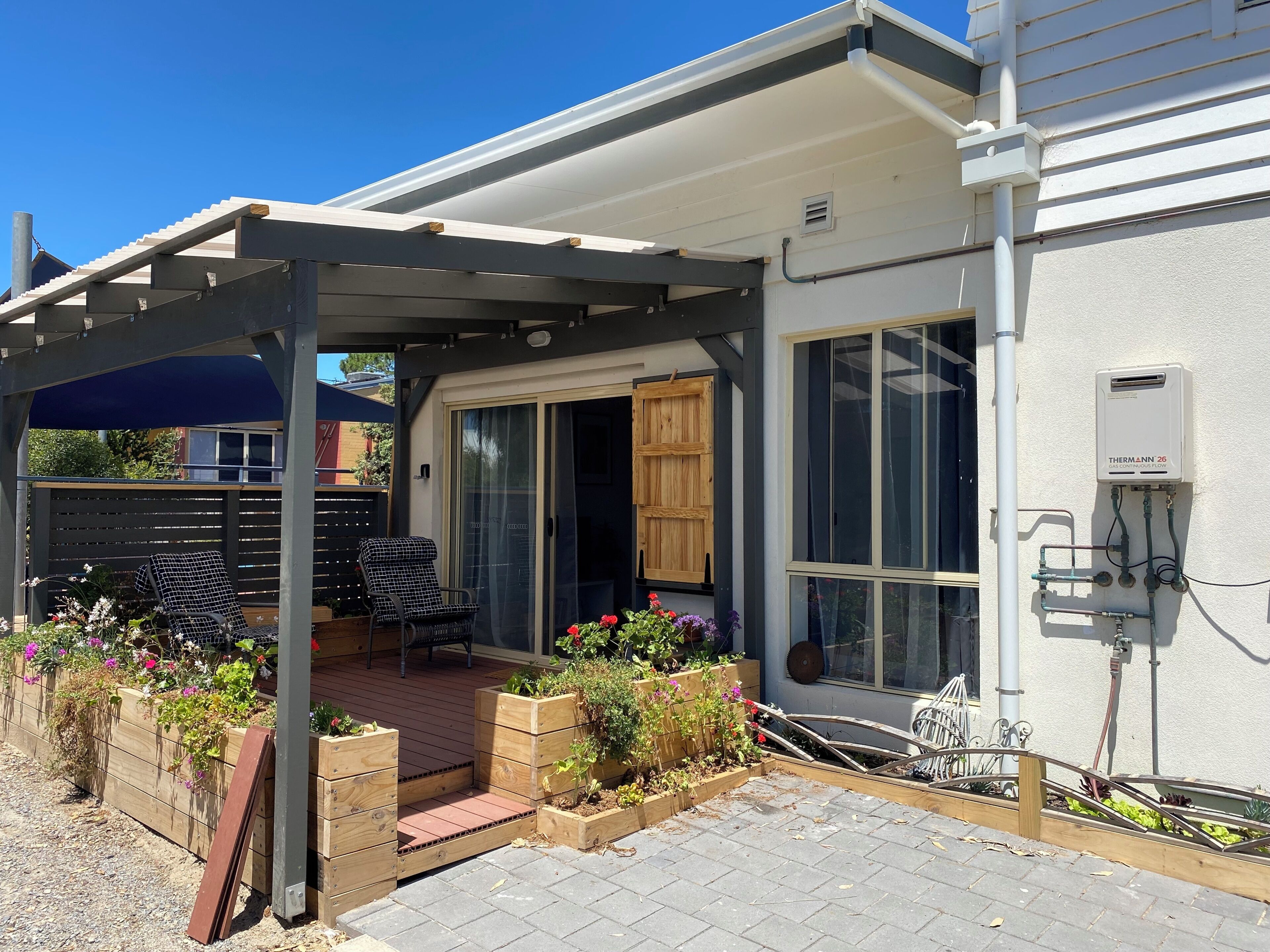 A covered patio area with a pergola, outdoor seating, and raised garden beds with flowers.