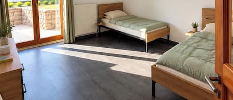 A bedroom with two beds, a desk, and a view of the outdoors through a sliding door.