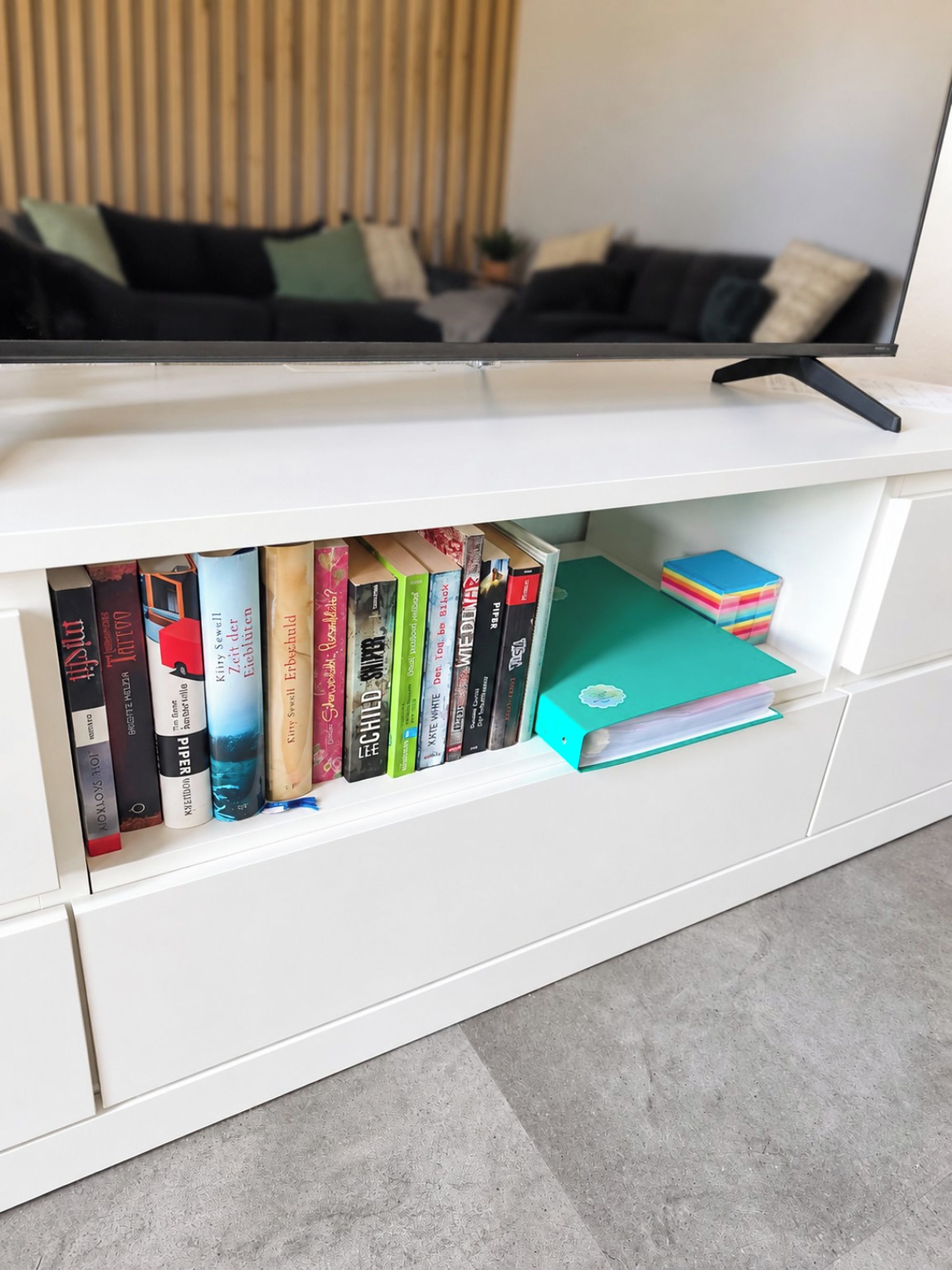 Eine weiße Unterhaltungsanlage mit Fernseher obenauf und einem Bücherregal darunter.