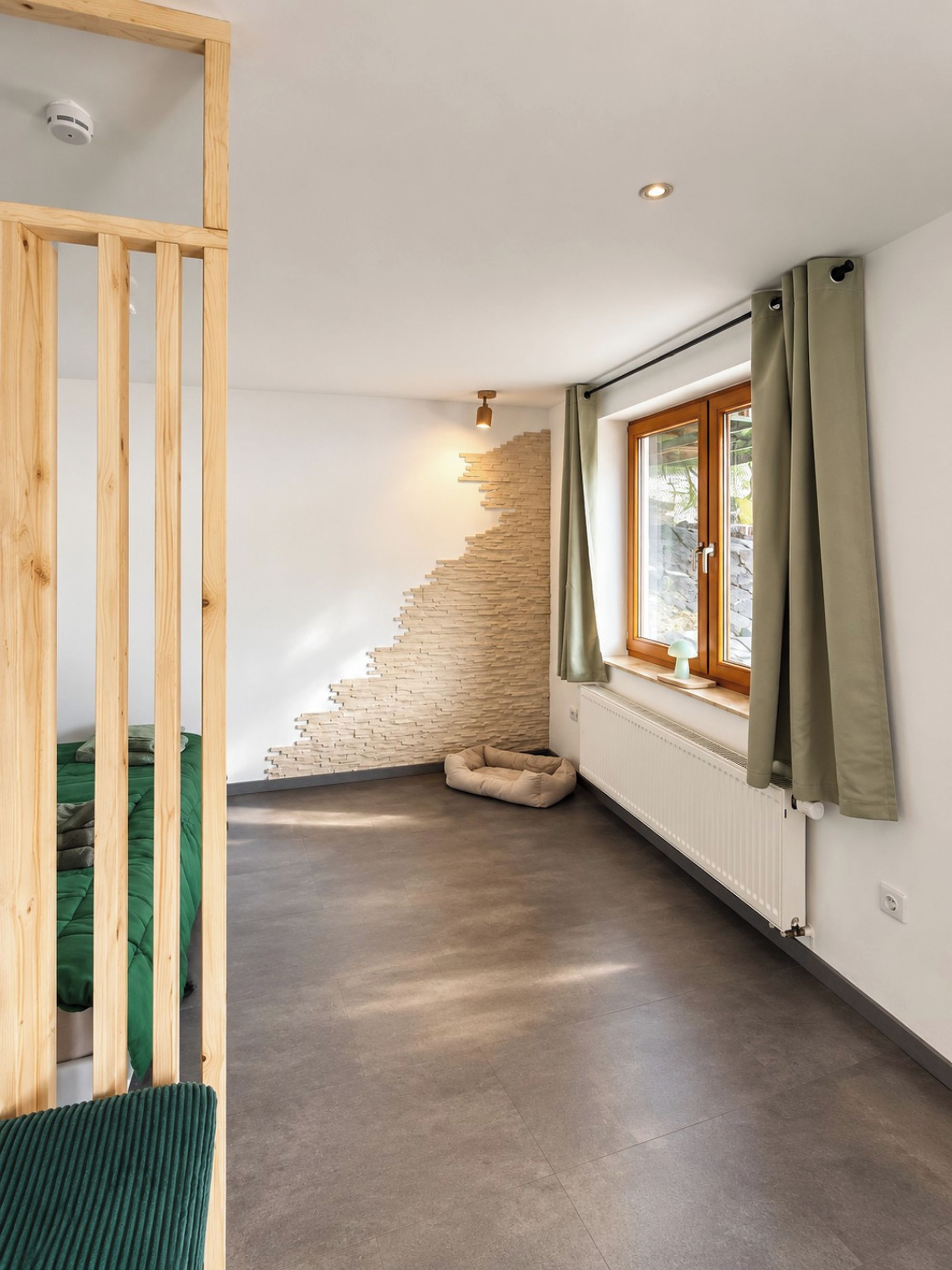 Ein Zimmer mit schrägem Dach, einem Platz für Haustiere, einem Fenster mit Vorhängen und einer Heizung.