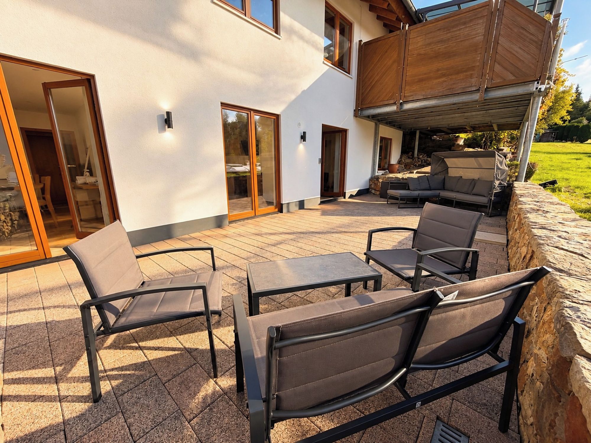 Eine Terrasse im Freien mit Sitzgelegenheit, darunter Stühle und ein Tisch, sowie ein überdachter Bereich mit Grill.