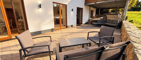 Een terras buiten, met een zithoek, inclusief stoelen en een tafel, en een overdekt gedeelte met een barbecue.