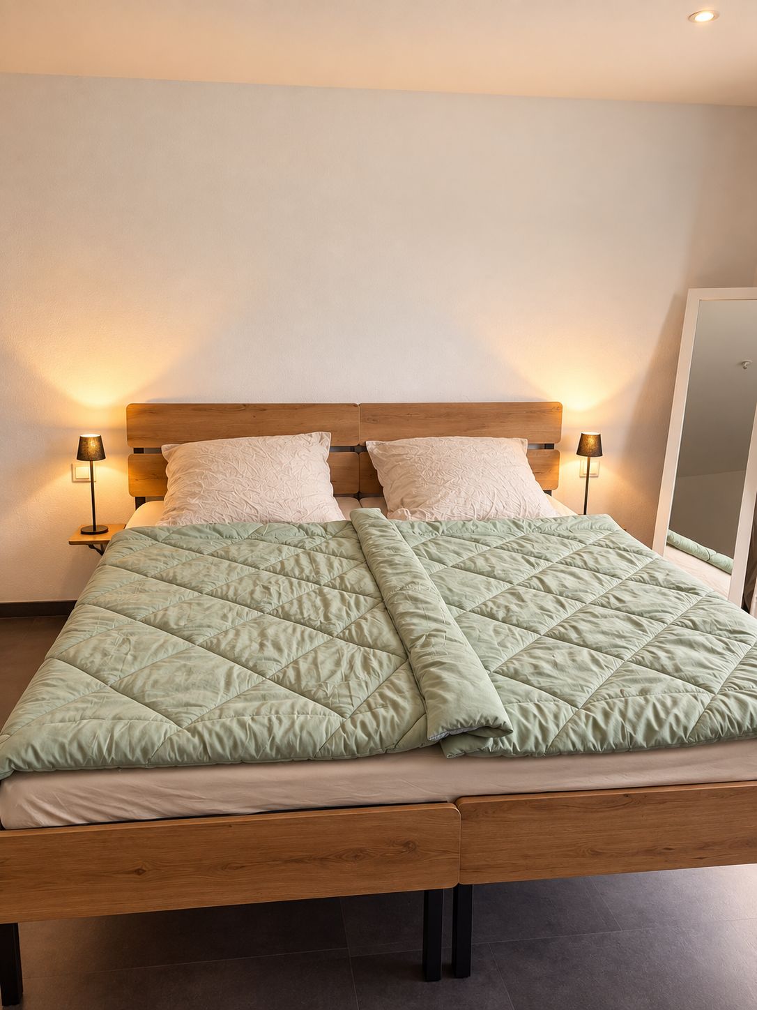 A bed with a wooden headboard, two bedside lamps, and a green quilted bedspread.