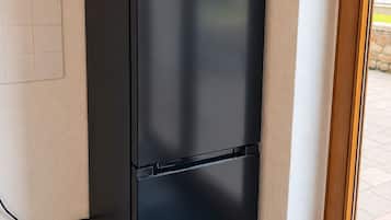 A black refrigerator with the brand 'comfee' in a corner of a room with tiled flooring and a window.