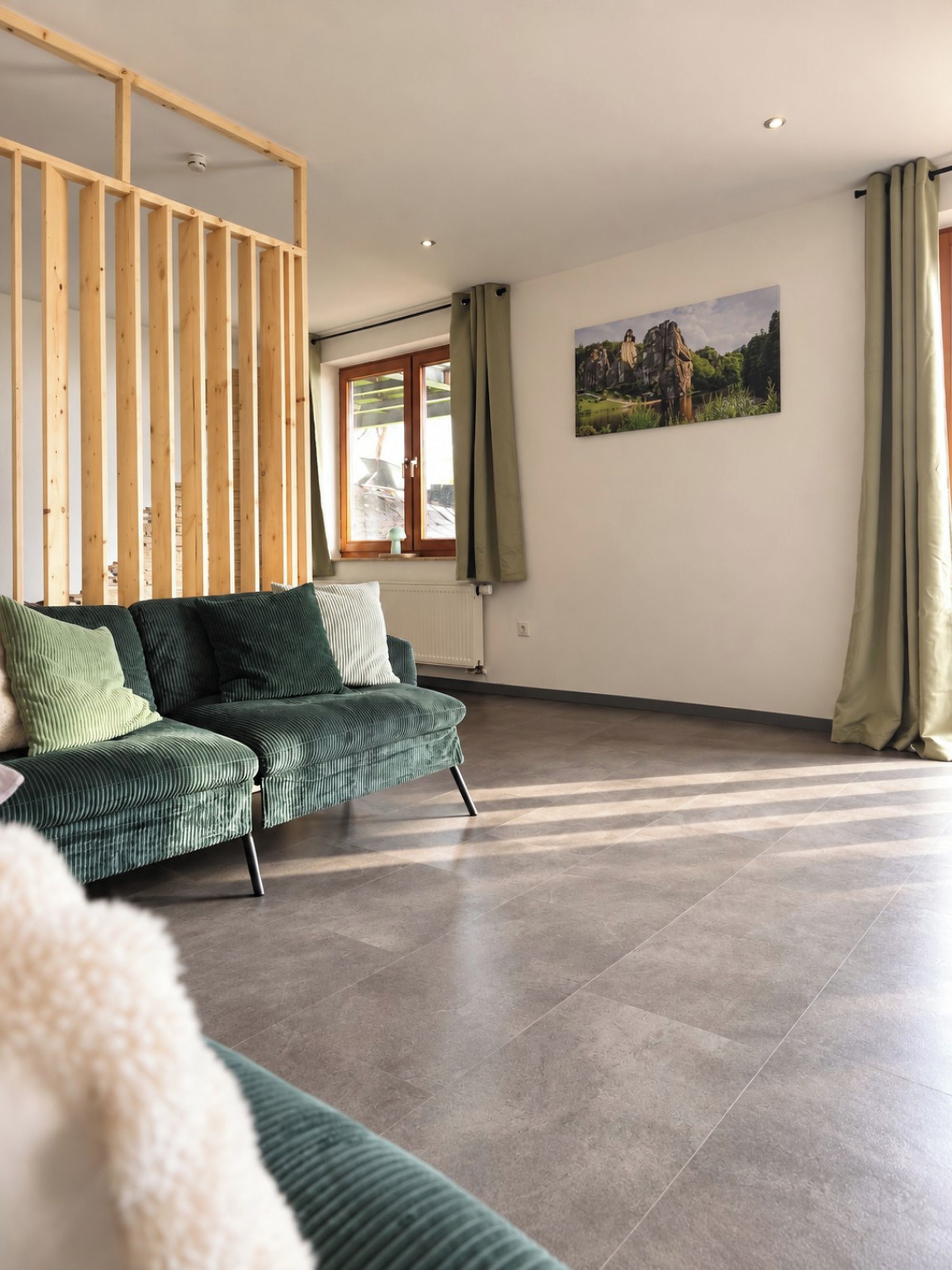 Ein modernes Wohnzimmer mit einem Ecksofa, einer Holzwand, einem großen Fenster mit Vorhängen und einem Gemälde an der Wand.