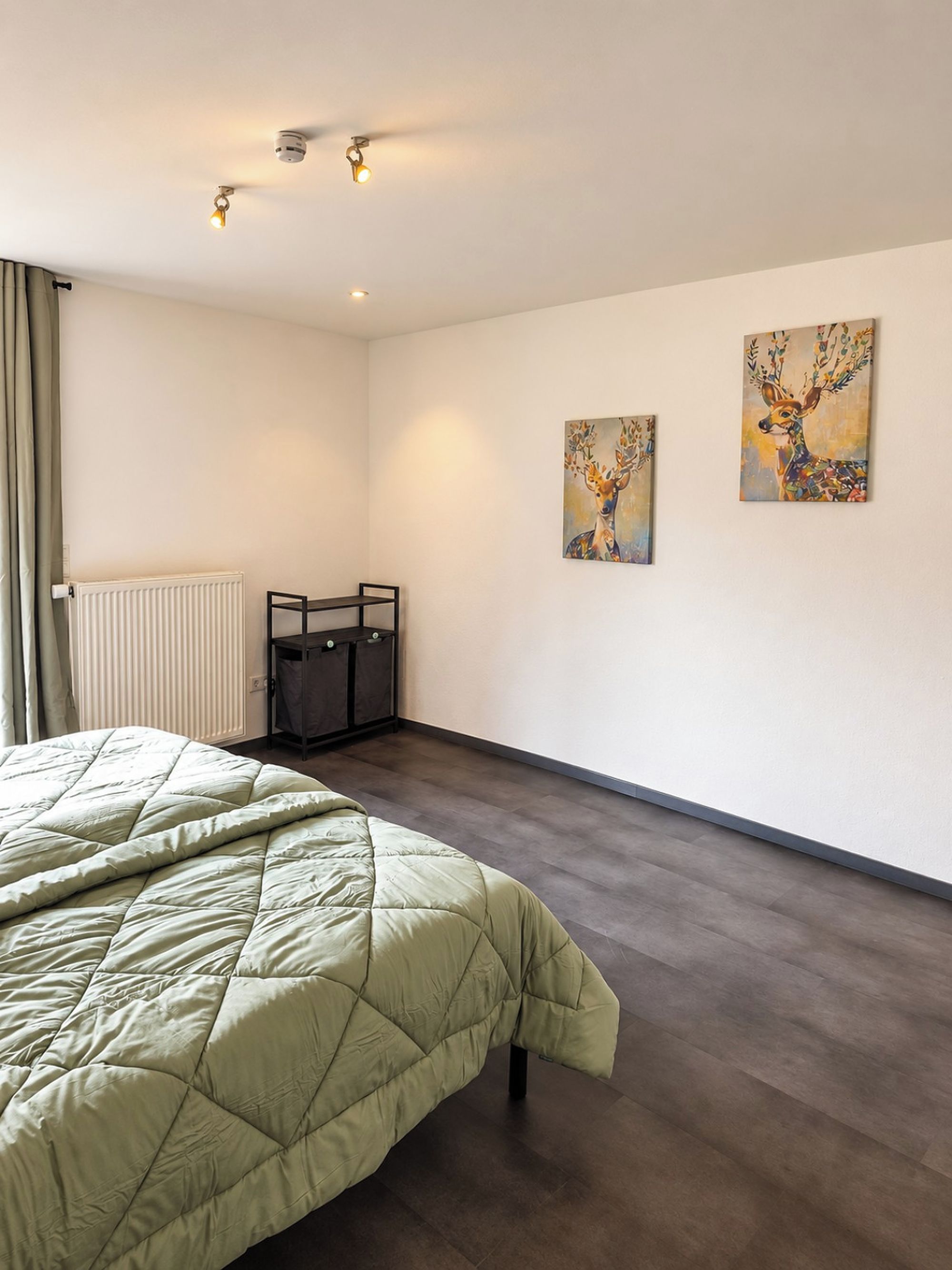 Ein Schlafzimmer mit einem Bett, einem Heizkörper, einem Schreibtisch und zwei an der Wand hängenden Bildern.