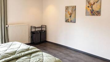 Ein Schlafzimmer mit einem Bett, einem Heizkörper, einem Schreibtisch und zwei an der Wand hängenden Bildern.