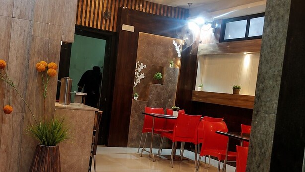 A hotel lobby with a reception desk, red chairs, a potted plant, and a tiled floor.