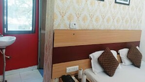 A hotel room with a wooden headboard, a bed with white and brown pillows, a small bedside table, and a window with a view of trees.