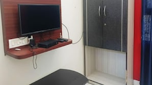 Una habitación con televisión montada en un estante de madera, un armario gris y una cortina roja.