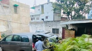 A residential area with a parked car, a person near a building, and potted plants.