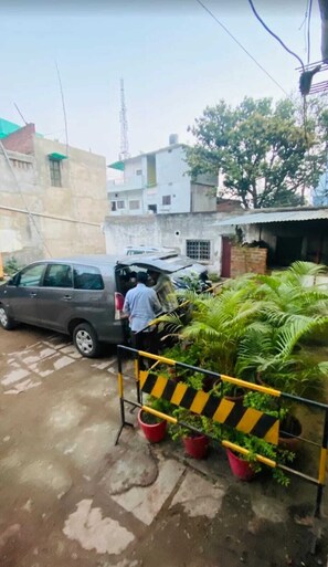 Zona residencial con un coche aparcado, una persona cerca de un edificio y plantas en macetas.