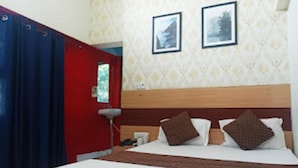 A hotel room with a bed, a nightstand, a lamp, and a red door.