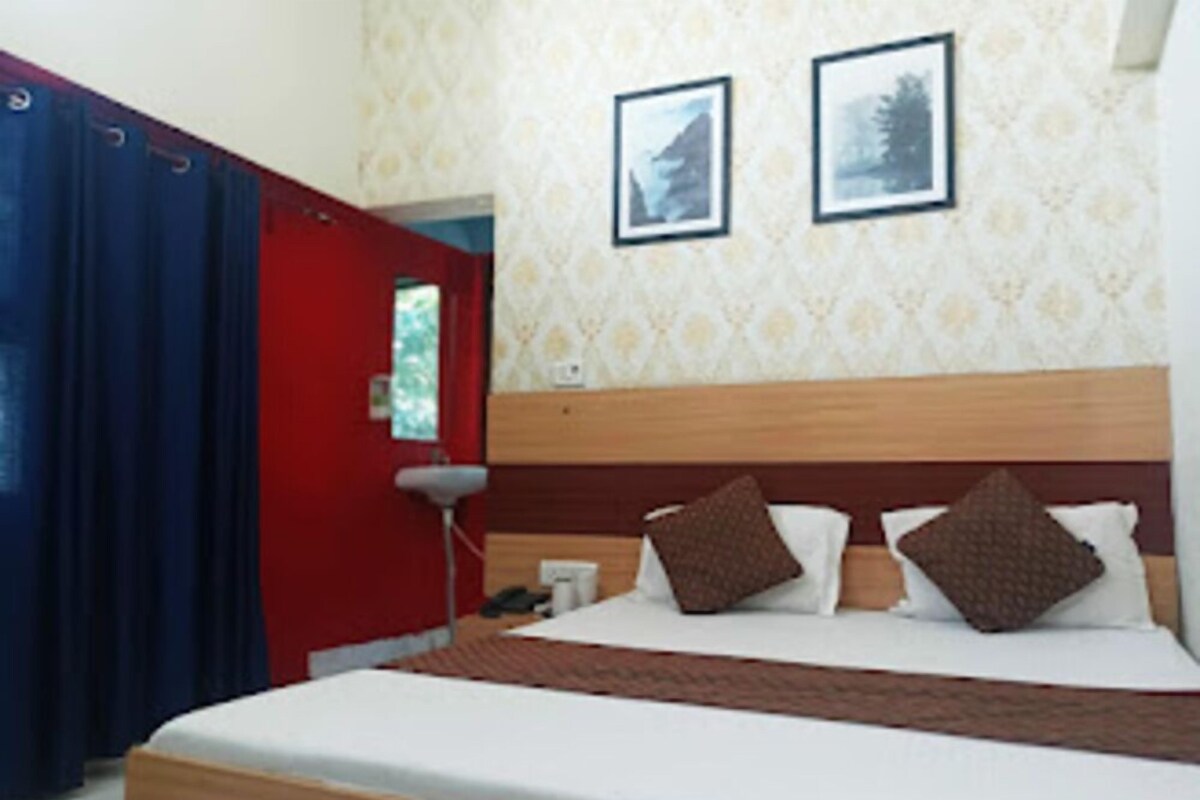 Una habitación de hotel con cama, mesita de noche, lámpara y puerta roja.