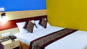 A hotel room with a bed, bedside table, lamp, and wall-mounted phone.