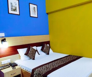 Una habitación de hotel con cama, mesita de noche, lámpara y teléfono en la pared.