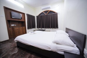 Een hotelkamer met een bed, een televisie bevestigd aan een houten kast en een airconditioning op de muur.
