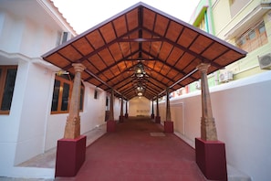 A covered walkway with a red floor, supported by columns, leading to a building entrance.